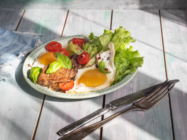 Fried eggs with fried liver on a round tray, served on a wooden board tray in the light of the sun's rays.