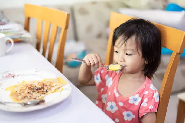Photo of Asian little baby child eating and enjoy breakfast by herself