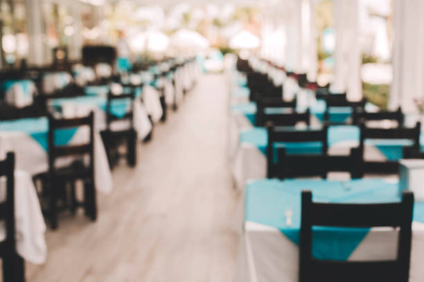 Abstract blur interior of a modern resort restaurant with blue tablecloths for background. Wooden floor, cozy vacation atmosphere, sunny summer day.