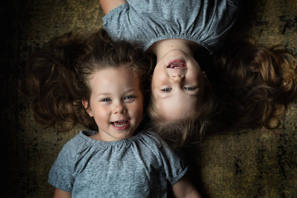 A portrait of identical twin toddler girls next to each other A portrait of identical twin toddler girls next to each other lying in different directions head to head with similar facial expressions gray eyes photos stock pictures, royalty-free photos & images