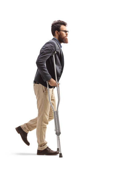 Full length profile shot of a young bearded man walking with crutches isolated on white background