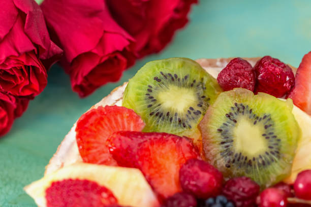 sweet cake with berries. strawberries, kiwi, currants, blackberries, raspberry, pineapple on the biscuit. fruit variety. dessert. bouquet of roses. soft focus. macro. top view. - biscuit red blue macro imagens e fotografias de stock