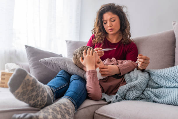 istock Sick boy with thermometer laying in bed and mother hand taking temperature 1147091301
