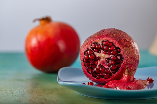 Pomegranate and red seeds of fruit on a blue plate. Beautiful bright tropical fruit on a green table. Closeup and soft focus.  Copy space