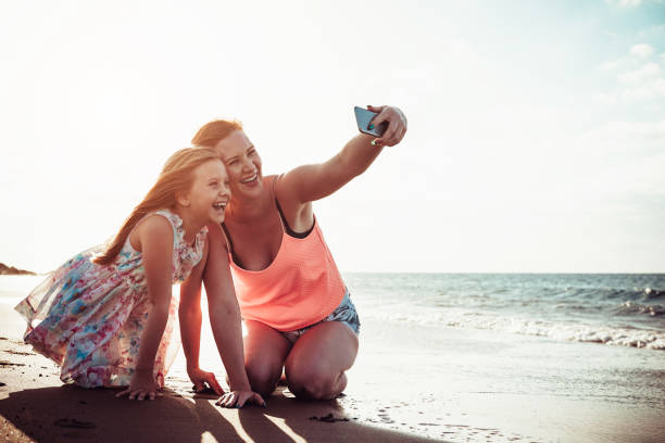 istock Mother and daughter taking selfie with mobile smartphone while playing on tropical beach at sunset - Happy family having fun with new technology apps for social media - Parenthood concept 1147108625