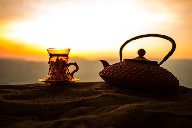 istock Arabic tea in traditional glass and pot on desert at sunset. Eastern tea concept. Artwork decoration on sand with tea. 1147111926