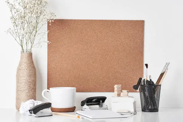Cork board with office supplies, cup and plant in bottle vase on white background. Home 
 office workplace