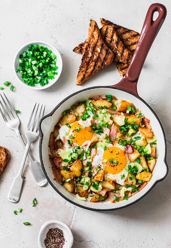 Potatoes, ham, eggs breakfast hash in a frying pan on a light background, top view. Delicious, nutritious breakfast, snack
