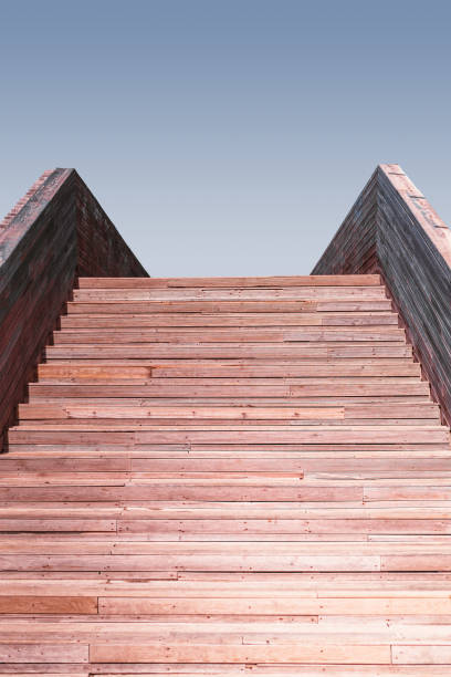 Vertical view of an outdoor wooden stair with a clear sky soft color gradient on the top, reddish tint of wooden steps