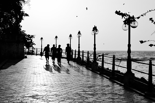 Mahe, Puducherry, India - January, 2017: Silhouettes of four men walking on the seafront park with paved walkway and street lights.