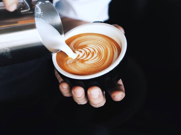 Close barista hands pouring milk in coffee cup.