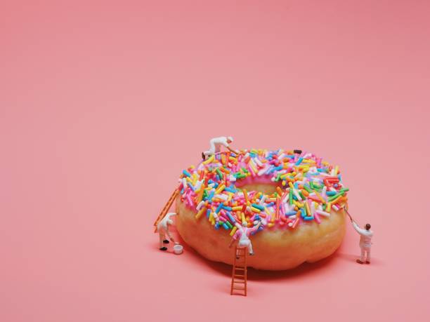 les gens miniatures peinture couleur sur le donut. - figurine photos et images de collection