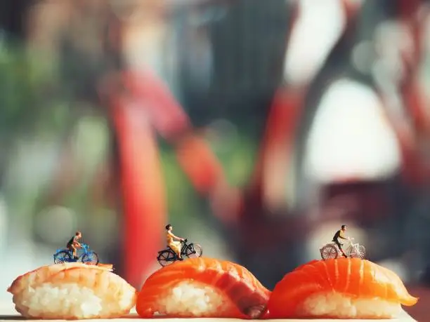 Photo of Miniature people riding bicycle on salmon sushi.