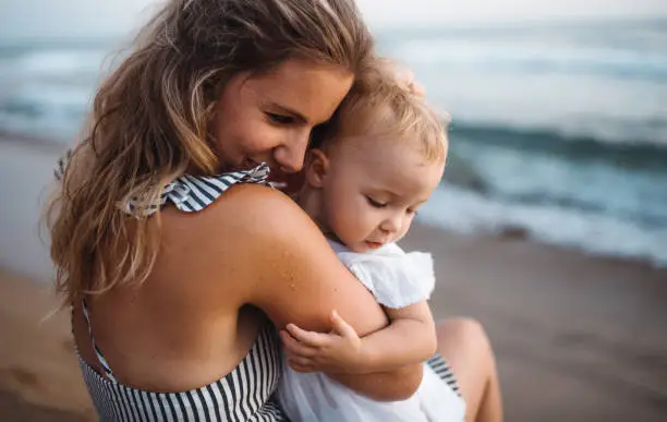 Photo of Close-up of young mother with a toddler girl on beach on summer holiday.