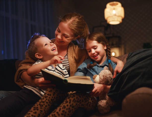 lettura serale in famiglia. madre legge i bambini . prenotare prima di andare a letto - bedtime stories foto e immagini stock