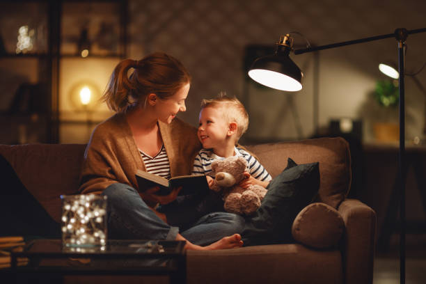 familie vor dem schlafengehen mutter liest zu ihrem kind sohn buch in der nähe einer lampe am abend - lichtquelle stock-fotos und bilder