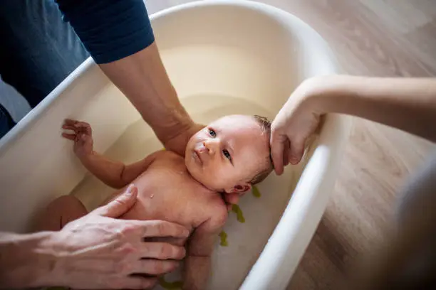 Photo of Unrecognizable parents giving a newborn baby a bath at home.