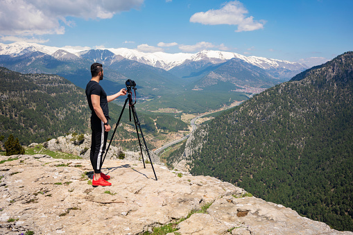 Photographer working with tripod and dslr camera on top of mountain.