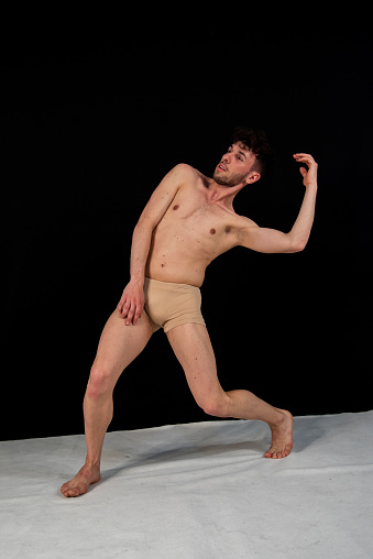 The attractive young man shows modern dance poses, on a black background.