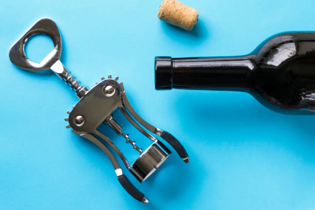 A corkscrew, a cork and a dark bottle of wine against a blue background. A corkscrew, a cork and a dark bottle of wine against a blue background. cork puller stock pictures, royalty-free photos & images