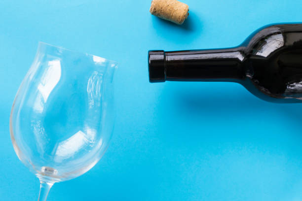 Dark bottle of wine, empty wine glass and cork on a blue background. Dark bottle of wine, empty wine glass and cork on a blue background. cork puller stock pictures, royalty-free photos & images