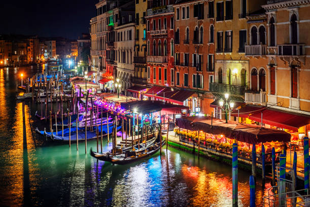 View of historical buildings, restaurants and gondolas at night from Rialto bridge, Venice, Italy.