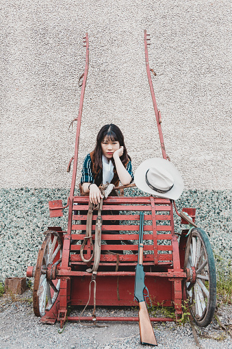 Portrait of a beautiful armed Chinese female cowgirl posing near an old carriage