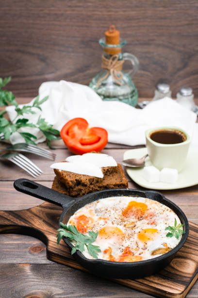 istock Ready-to-eat breakfast: shakshuka from fried eggs with tomatoes and parsley in a pan, bread with butter and coffeee 1147149960