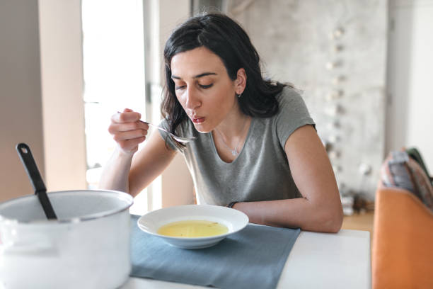 Young Woman Sick At Home Young woman sick at home eating soup. soup stock pictures, royalty-free photos & images