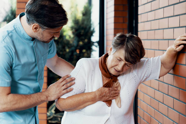 male nurse helping sick elderly woman with chest pain - nurse illness doctor heart disease imagens e fotografias de stock