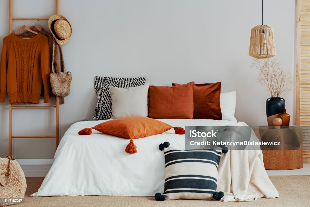 Colorful pillows on white bed of classy bedroom with round wooden bedside table and ladder Autumn Stock Photo