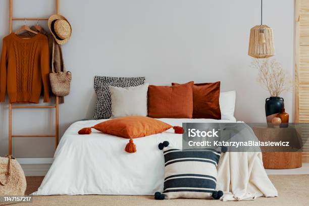 Colorful Pillows On White Bed Of Classy Bedroom With Round Wooden Bedside Table And Ladder Stock Photo - Download Image Now