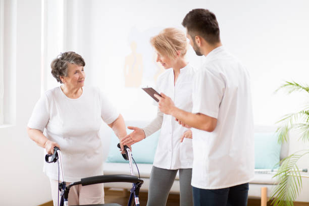 donna anziana grigia con deambulatore durante la fisioterapia con medico femminile professionista e infermiera maschile - doctor old male family foto e immagini stock