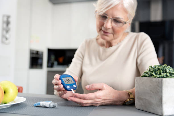 donna anziana che controlla il livello di zucchero nel sangue a casa - diabetes foto e immagini stock