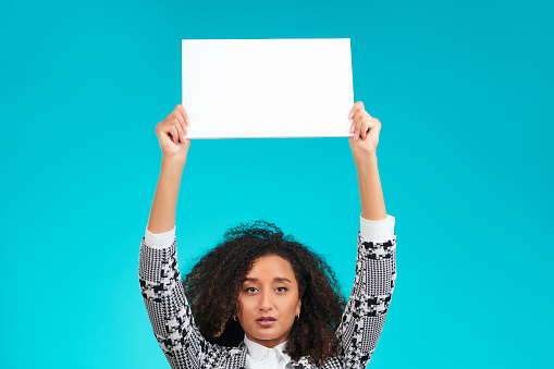 Office woman holding sign. Afro American business woman, holding a white board in her hands for your message. Copy space left for a message. Pastel blue colored background.