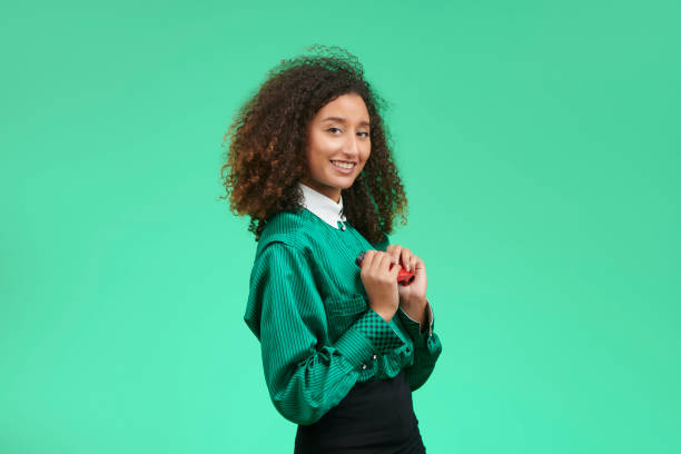 Education, people, children and school concept - young school girl sitting on desk with a book on her head over green