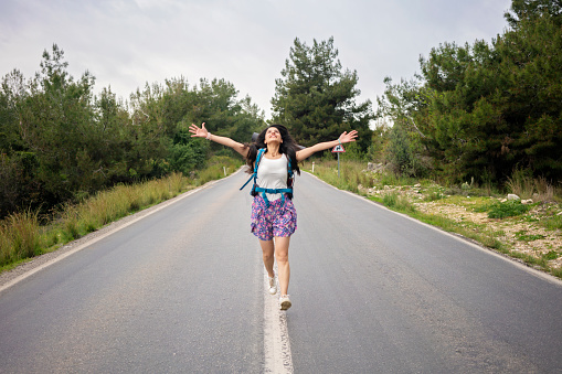 Young woman hiker or backpacker running on asphalt road in nature for freedom.