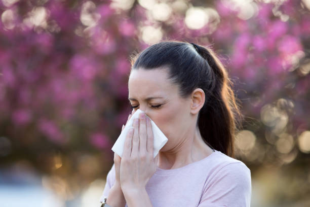 Girl having allergy symptoms in spring Young pretty woman blowing nose in front of blooming tree. Spring allergy concept allergy stock pictures, royalty-free photos & images