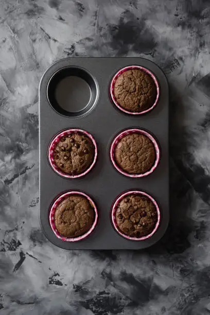 Delicious chocolate muffins in baking tin on dark background top view copy space