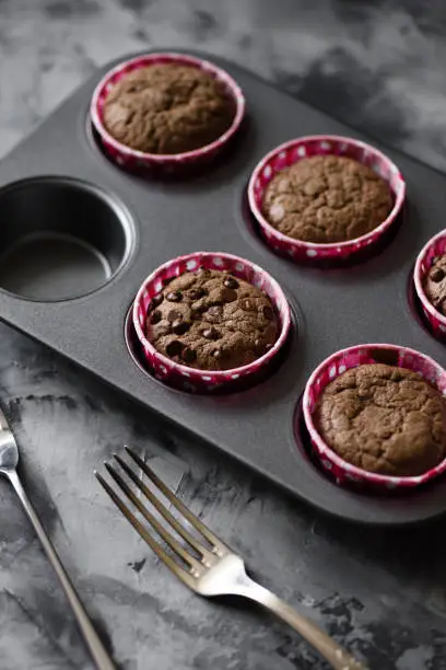 Tasty homemade pastry. Chocolate muffins in baking tin on dark background side view