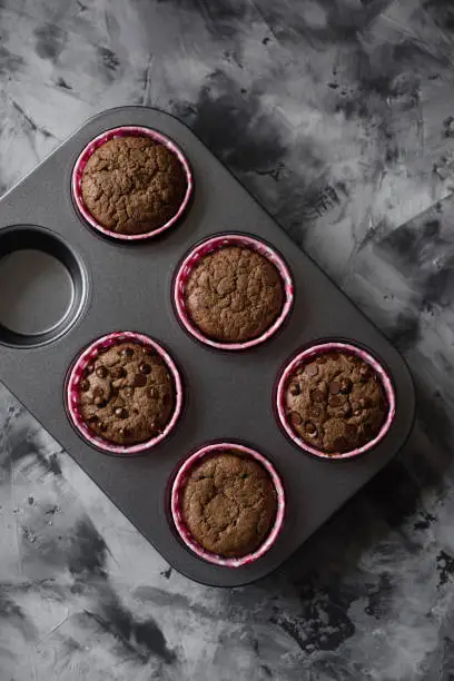 Tasty homemade chocolate muffins in baking tin on dark background top view copy space