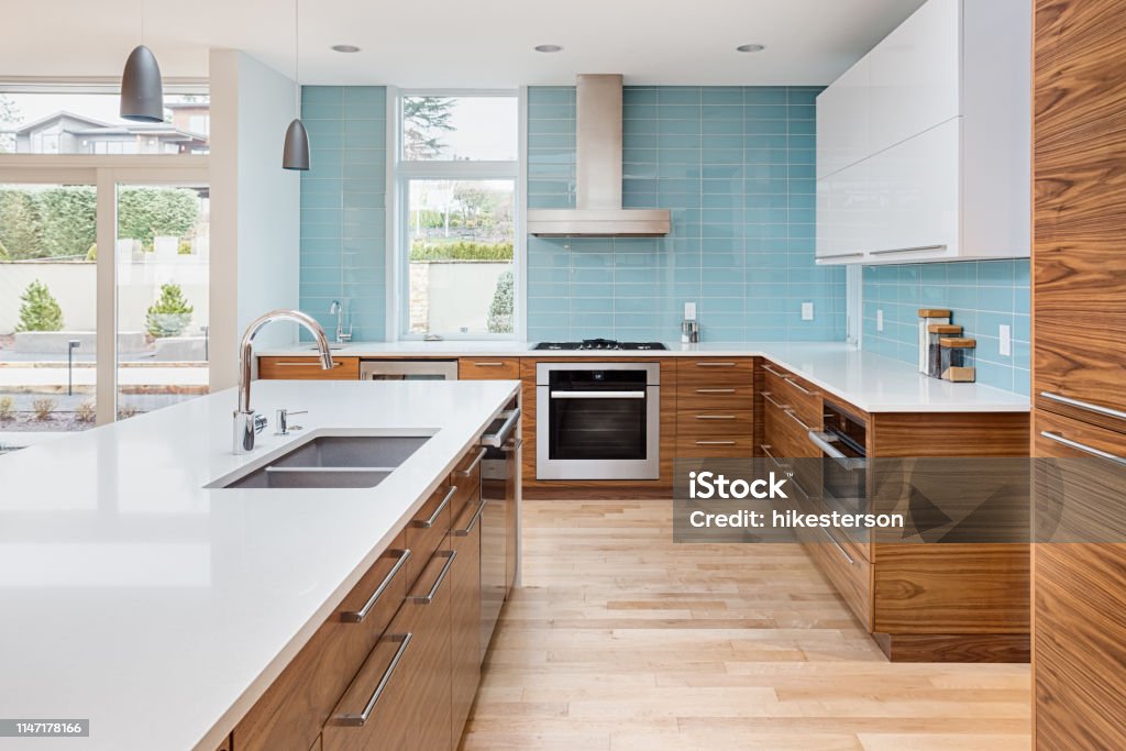 beautiful modern kitchen in new contemporary style luxury home, with island, pendant lights, hardwood floors, and stainless steel appliances. Features blue tone tile that extends to the ceiling kitchen in newly constructed luxury home Kitchen Stock Photo