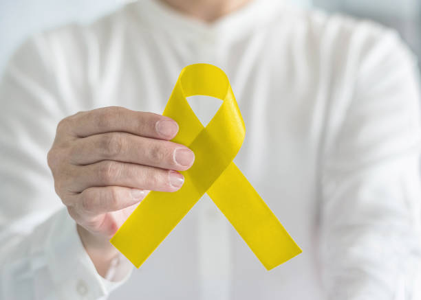 Yellow ribbon symbolic color for suicide prevention and Sarcoma Bone cancer awareness in person's hand Yellow ribbon symbolic color for suicide prevention and Sarcoma Bone cancer awareness in person's hand bladder cancer stock pictures, royalty-free photos & images