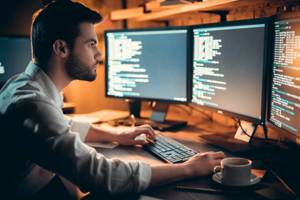 Focused developer coding on computer monitors working late in office Focused young developer coding late in office writing script shown on computer monitors, serious handsome coder programmer hacker programming developing software applications working alone at night computer language stock pictures, royalty-free photos & images