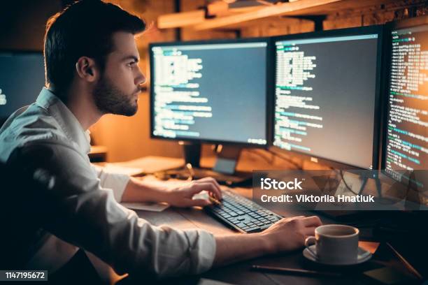 Focused Developer Coding On Computer Monitors Working Late In Office Stock Photo - Download Image Now