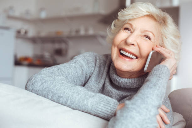 bella nonna in maglione grigio che parla al telefono - grandmother senior adult family domestic kitchen foto e immagini stock