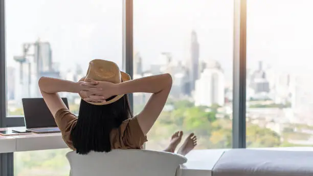 Work and travel lifestyle relaxation and healthy work-life balance with young freelancer Asian working woman take it easy happily resting in comfort luxurious hotel guest room with peace of mind