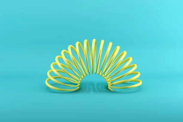 Photo of Yellow slinky isolated on blue background. Minimal conceptual idea concept.