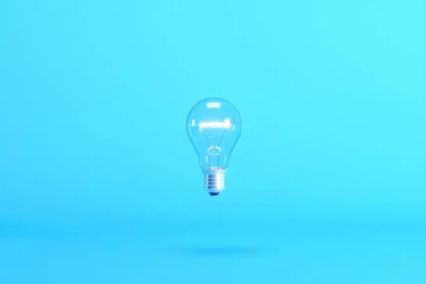 Photo of Floating light bulb isolated on blue background. Minimal conceptual idea concept.