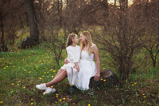 Mom and child are relax on the meadow among forest flowers. Girl sits in her mother's lap. Time together. Mother's Day. Mother and daughter looking at each other's eyes